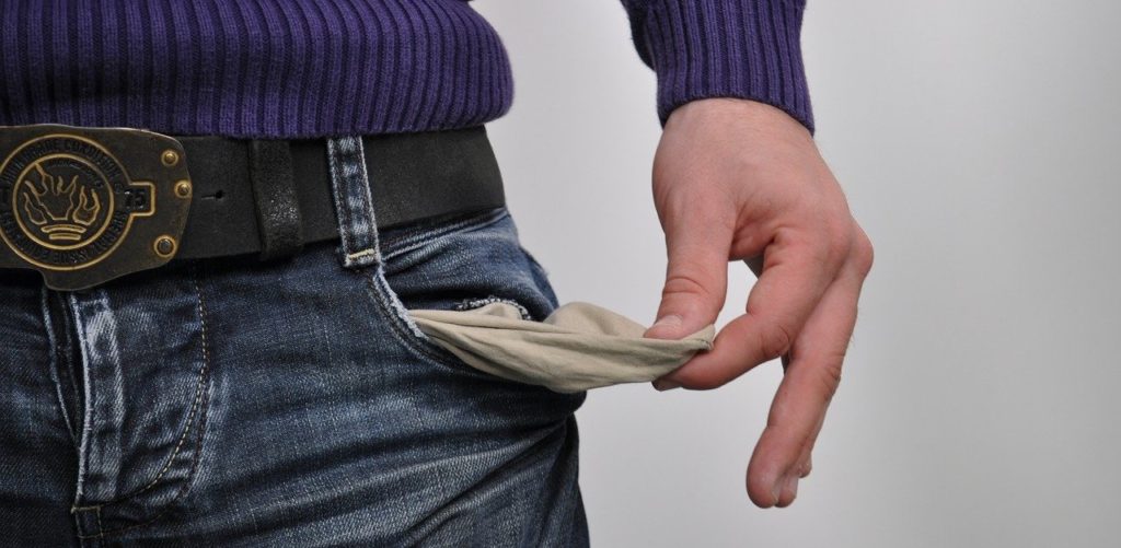 A man's hand pulling his pocket inside out to show he has no money