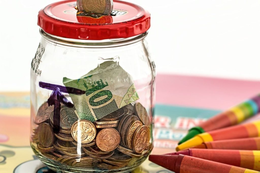 a jar half full of coins and bills. Crayons lay on the table next to the jar