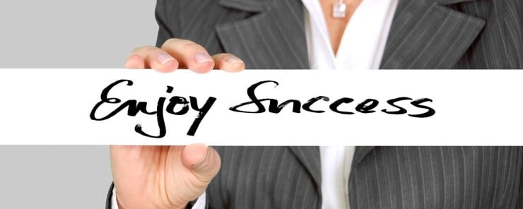 A close up of a woman in a business suit holds up a sign that says Enjoy Success.